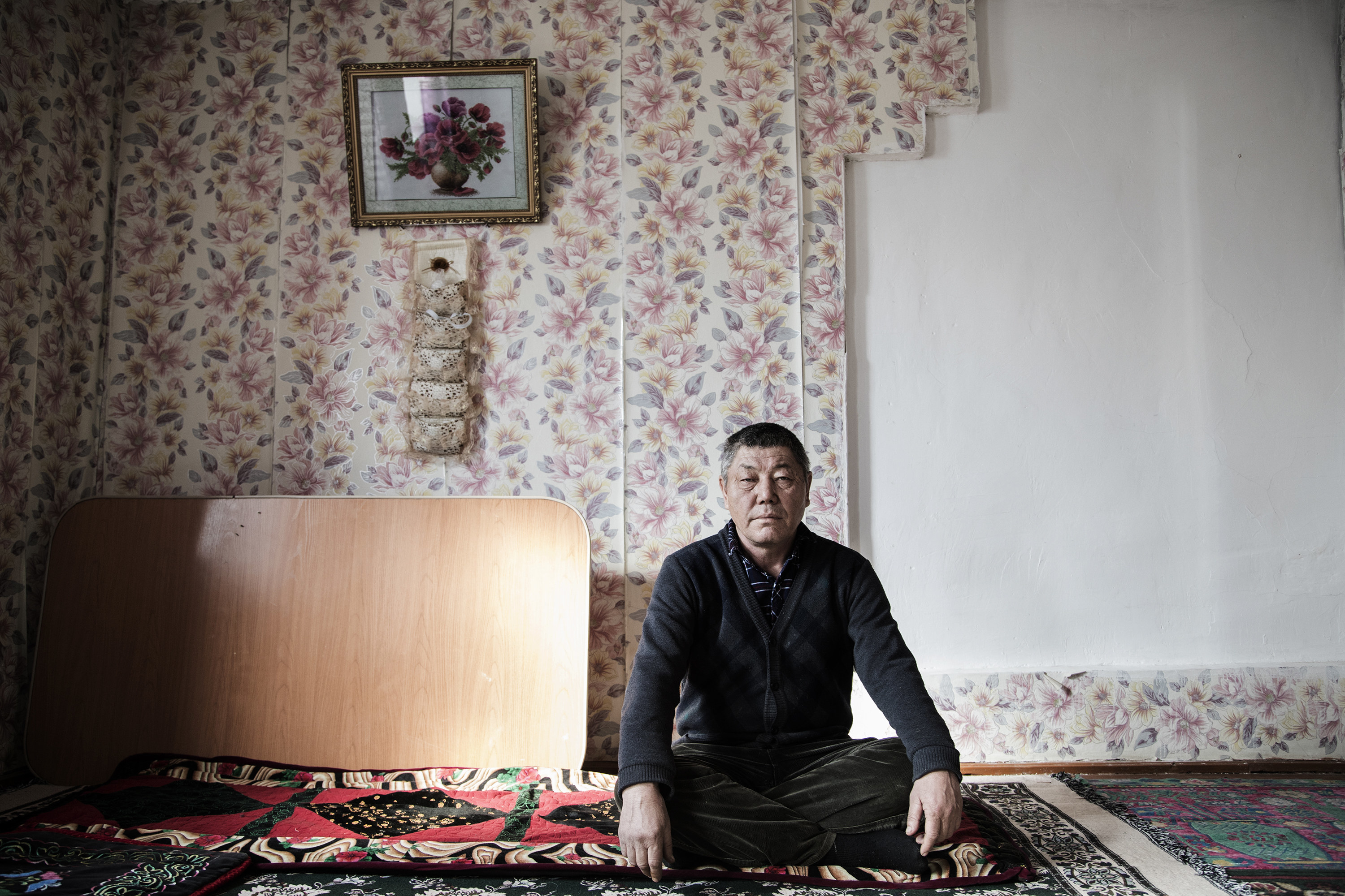A Uighur man sitting on the floor with his hands on his knees